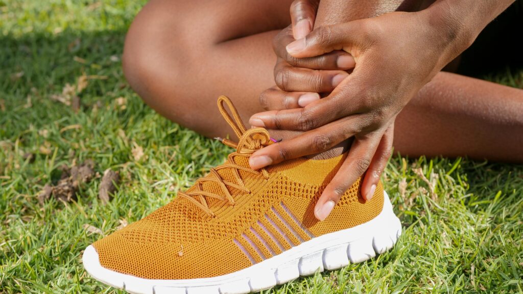 pexels-photo-7298647-7298647 Close-up of athlete holding ankle with running shoe on grass, indicating pain or injury.